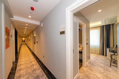 A hotel hallway with a marble floor, a door leading to a room, and a visible room number sign.