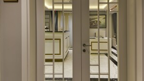 Puertas dobles con un panel de vidrio satinado, que dan acceso a una habitación con piso de mármol y un baño visible con bañera.