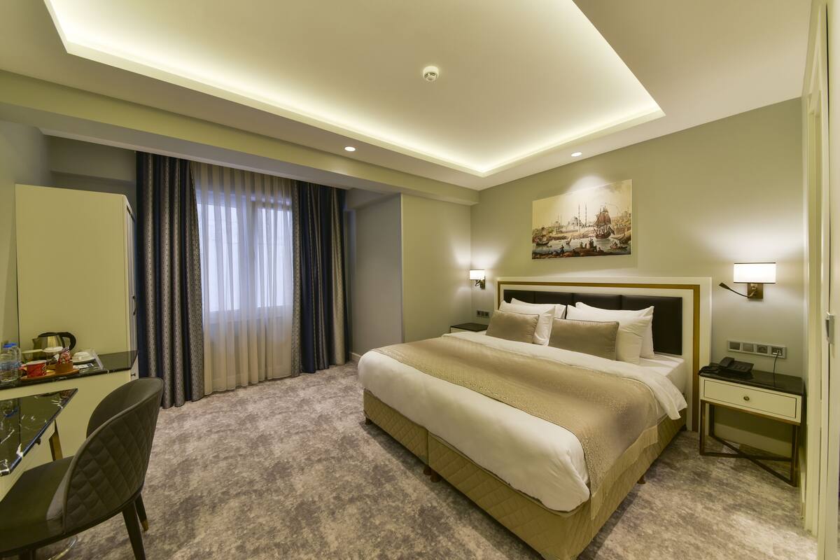 Une chambre d’hôtel avec un grand lit, des tables de chevet, un bureau avec une chaise et un tableau au mur.