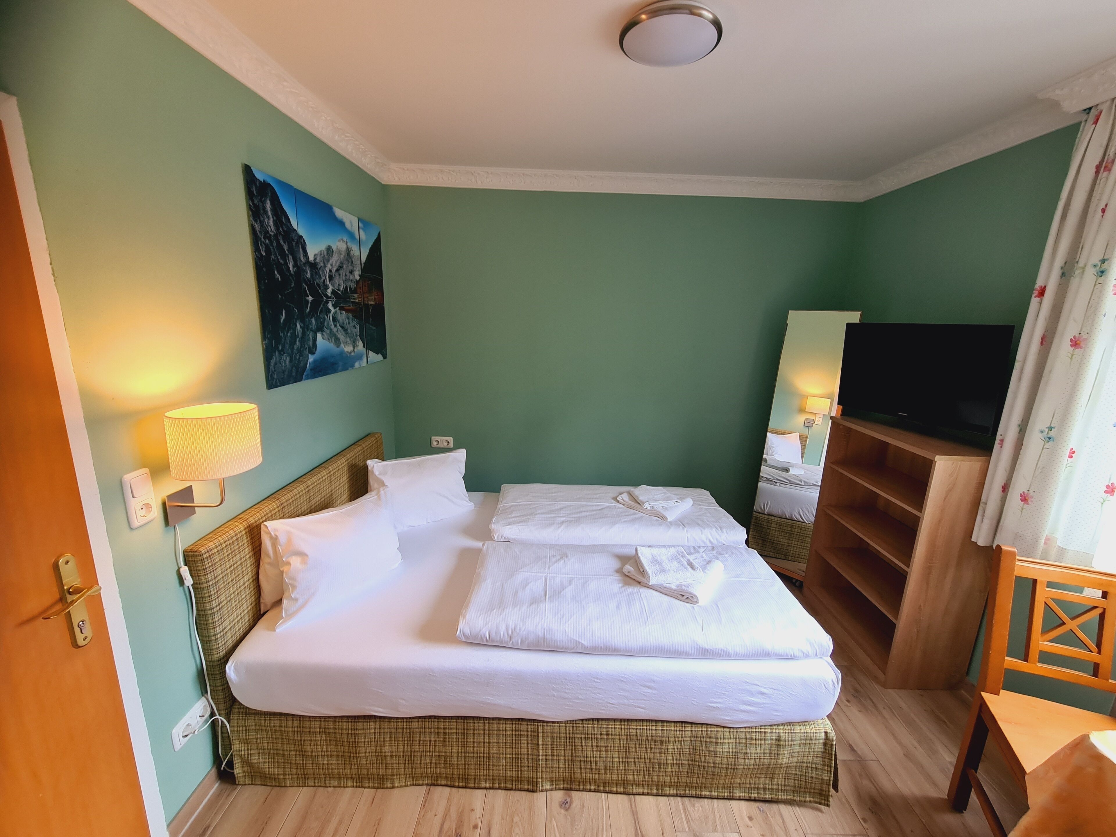 A hotel room with a bed, a television, a painting, and a lamp.