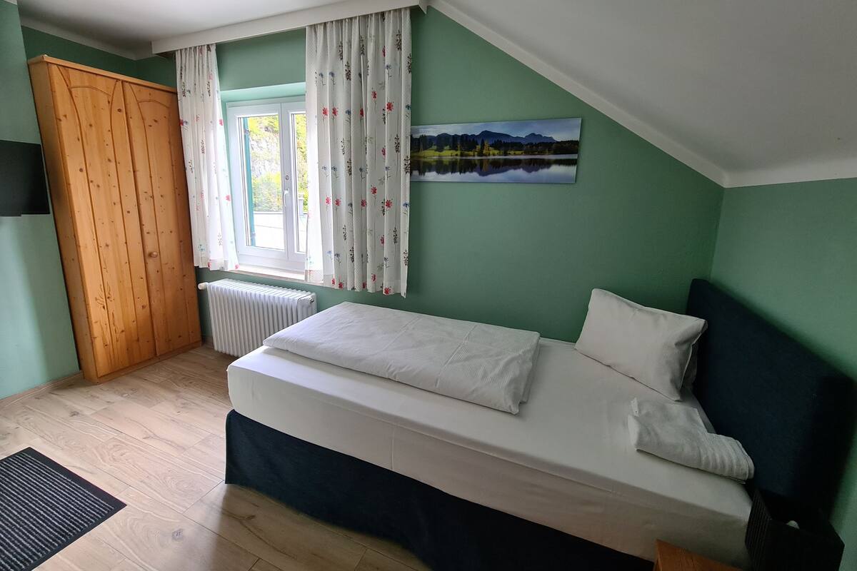 A bedroom with a bed, a window with curtains, a radiator, and a door.