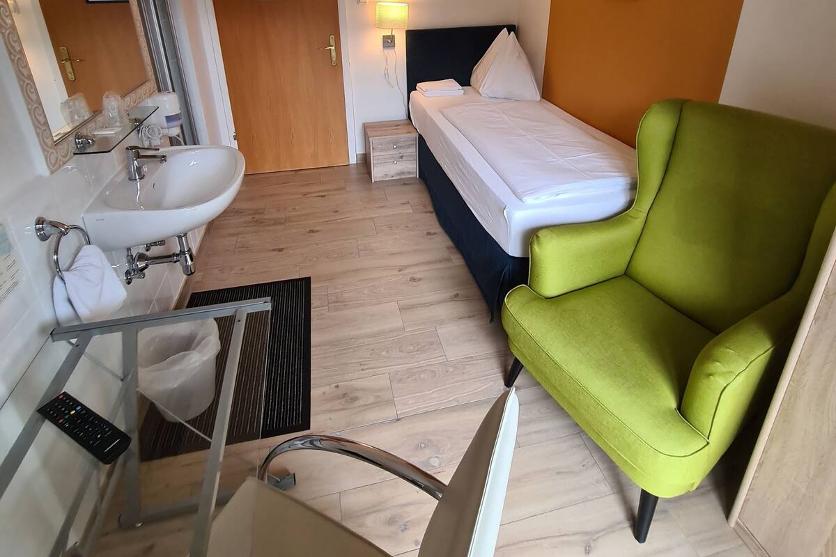A hotel room with a bathroom, a bed, and a green armchair.