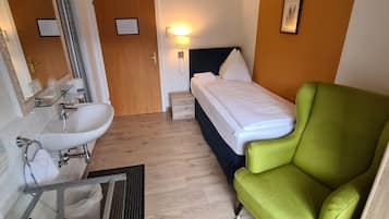 Et hotelværelse med badeværelse, seng og en grøn lænestol.