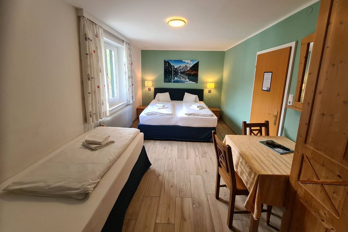 A small, well-lit room with two single beds, a wooden table, and a chair.