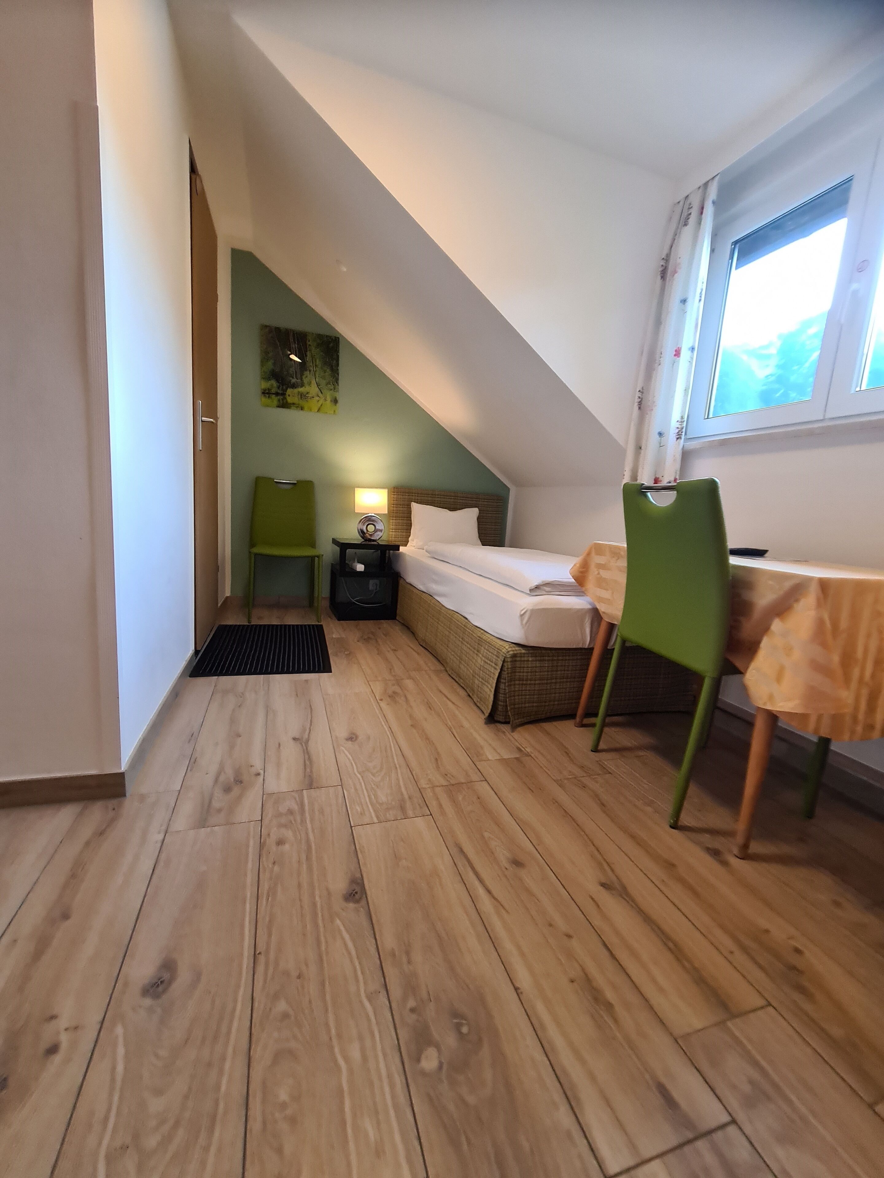 A small, cozy room with a bed, a chair, a table, and a window.