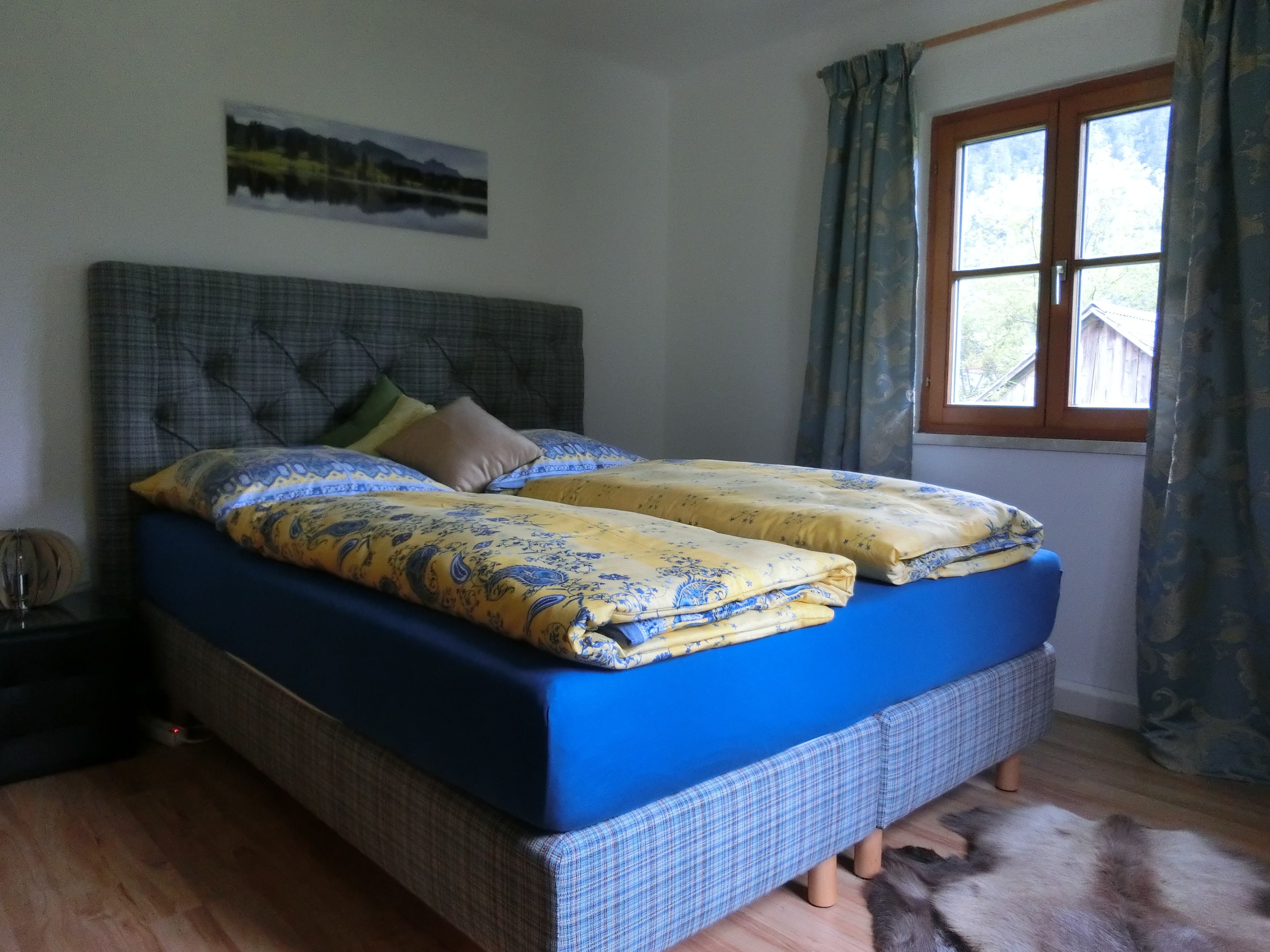 Ein Doppelbett mit blauer Bettwäsche, ein grauer Kopfteil und ein kleiner Nachttisch mit einer Lampe.