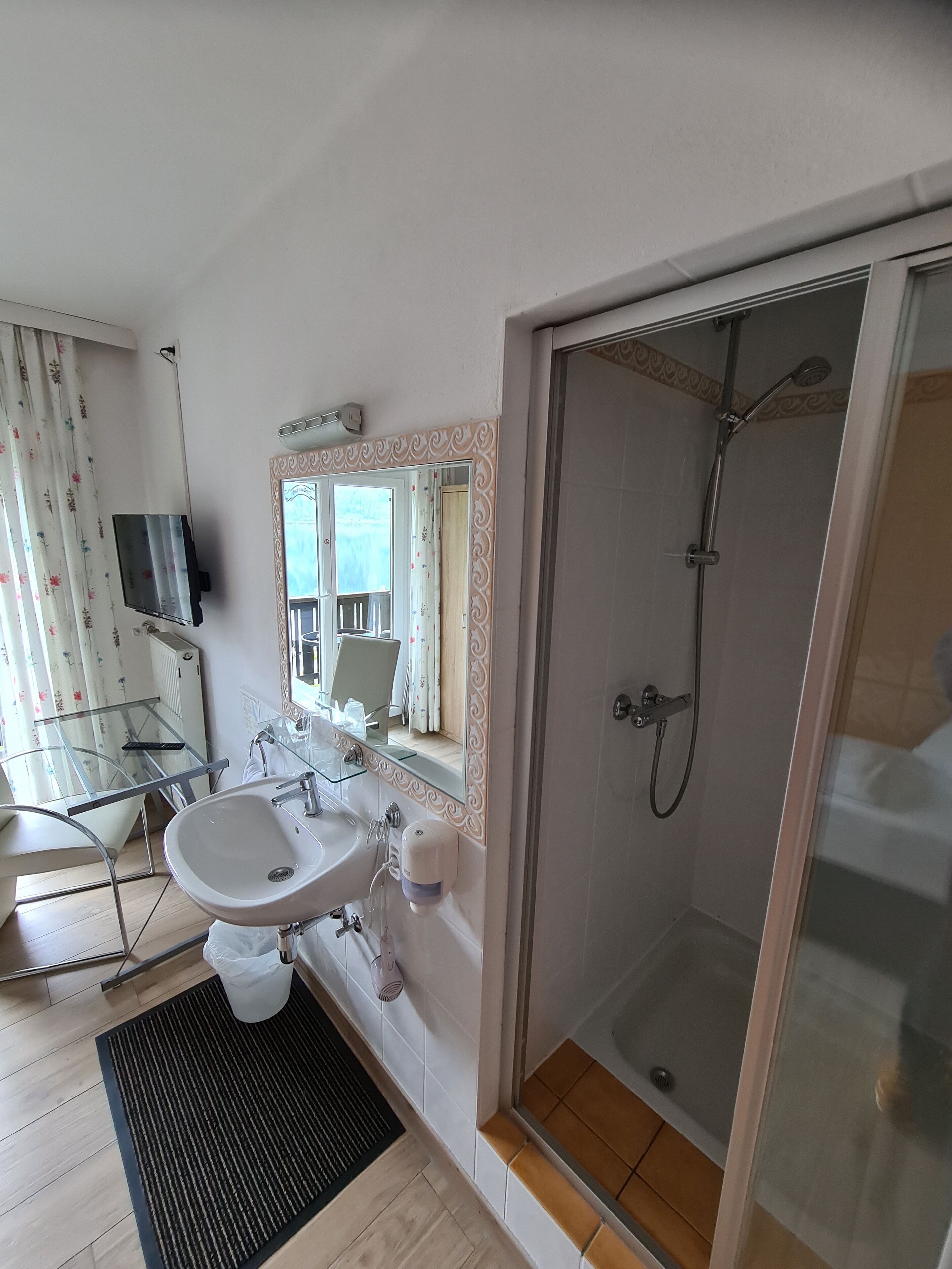 A modern bathroom with a glass shower enclosure, a sink with a mirror, and a glass door leading to a balcony.