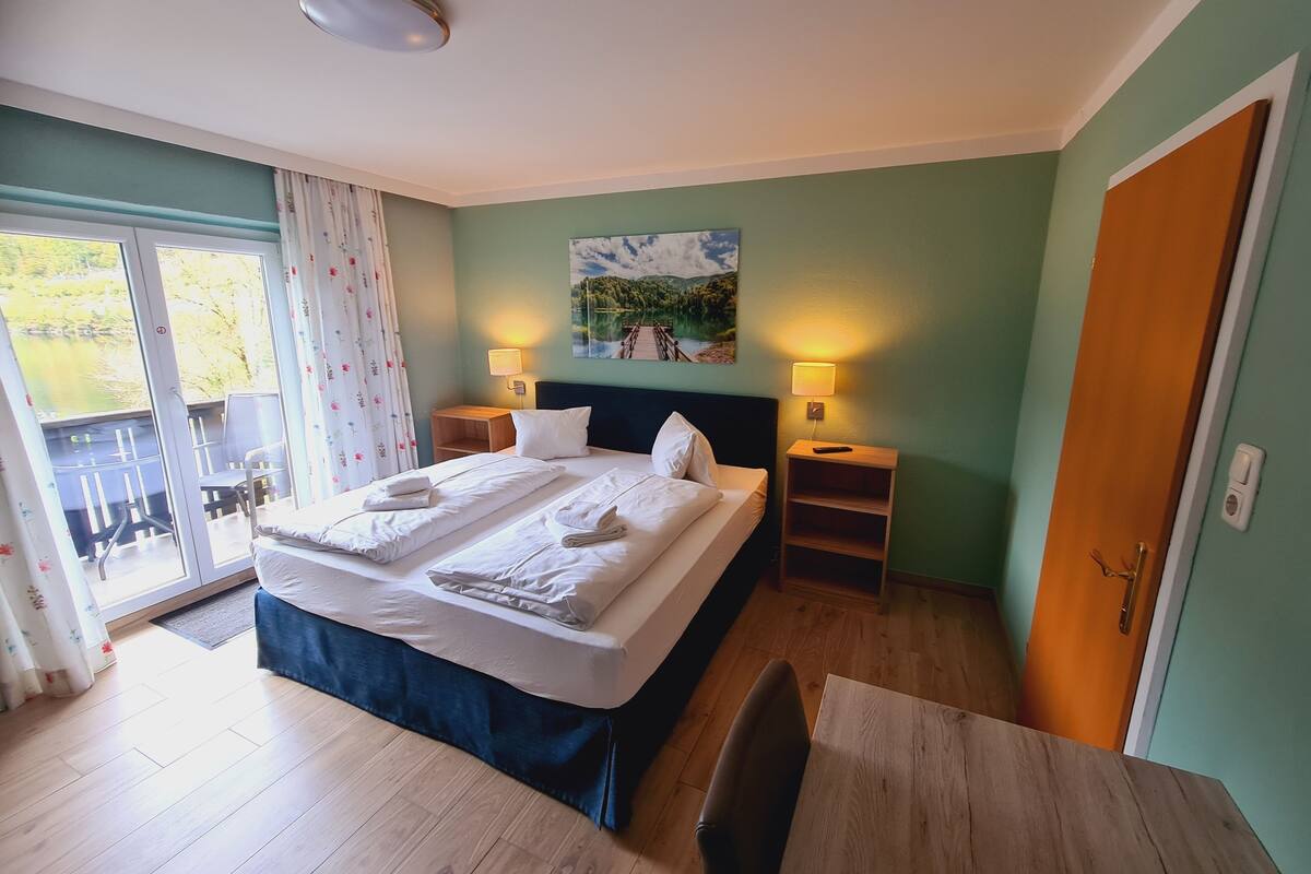 A hotel room with a large bed, two bedside tables with lamps, a painting on the wall, and a sliding glass door to the balcony.