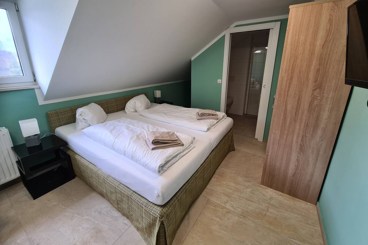 A bedroom with two beds, a nightstand, a lamp, and a view of the bathroom.