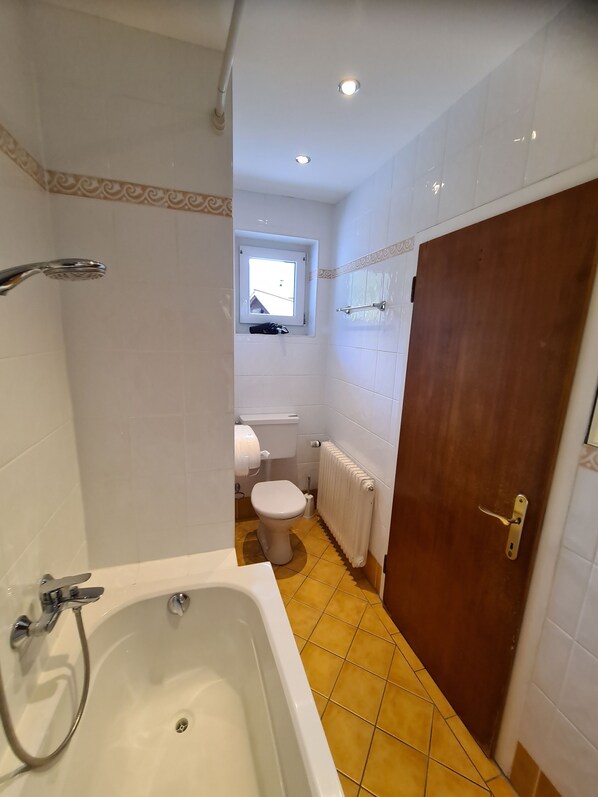 A bathroom with a bathtub, toilet, and a window. - Hotel Haus am See Self Check-in (Obertraun)