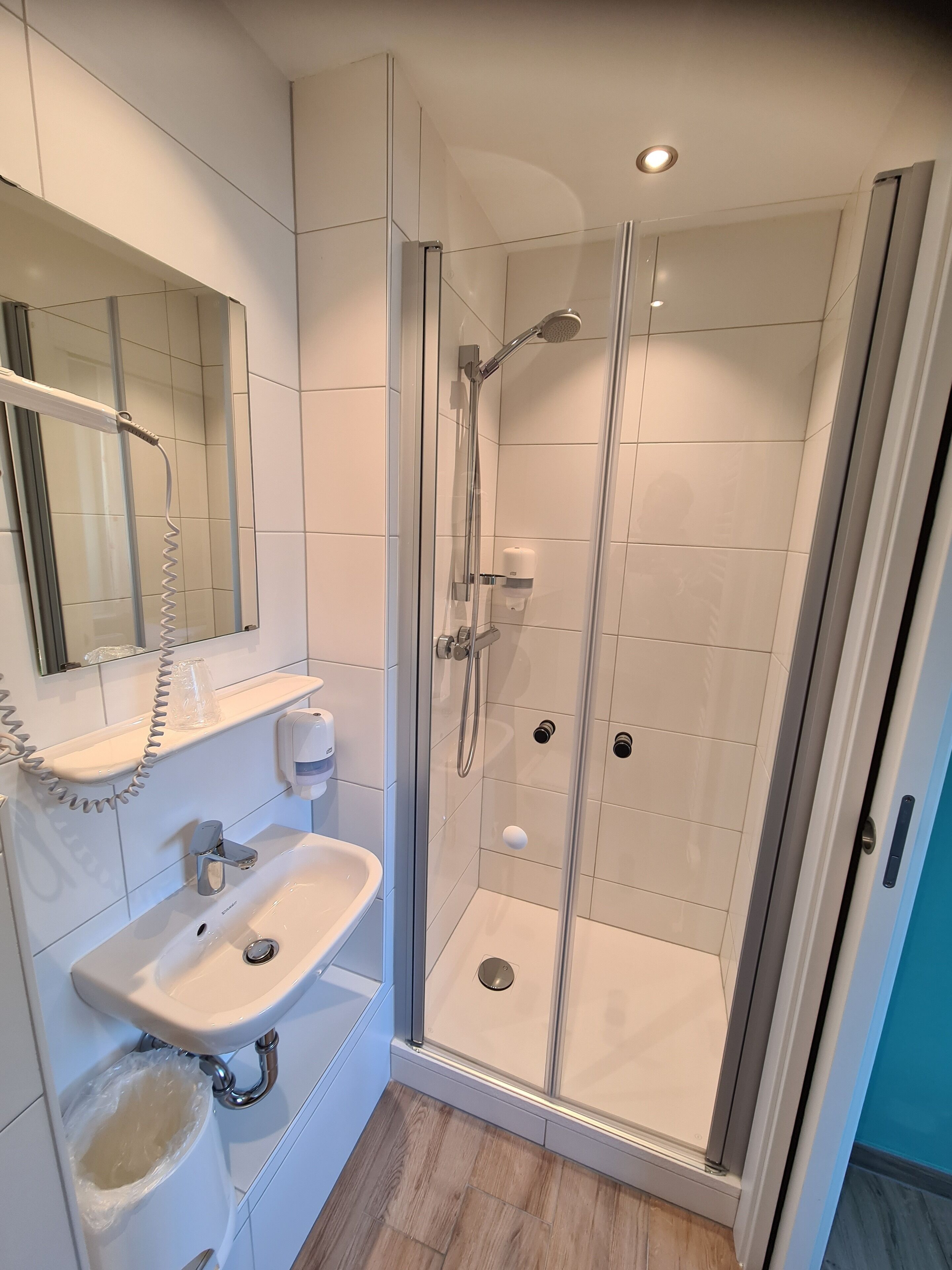 Ein modernes Badezimmer mit einer Duschkabine, einem weißen Waschbecken, einem Spiegel und einer Seifenspender.