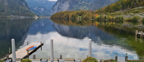 A lakeside patio with tables and chairs, surrounded by mountains and a dock with kayaks.