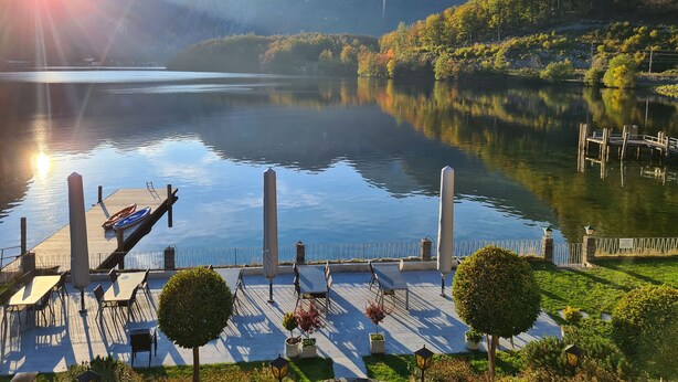 Un muelle a orillas del lago con mesas y sillas, rodeado de vegetación y montañas.