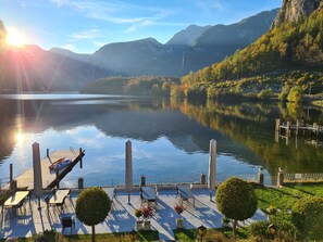 A lakeside dock with tables and chairs, surrounded by greenery and mountains. - Hotel Haus am See Self Check-in (Obertraun)