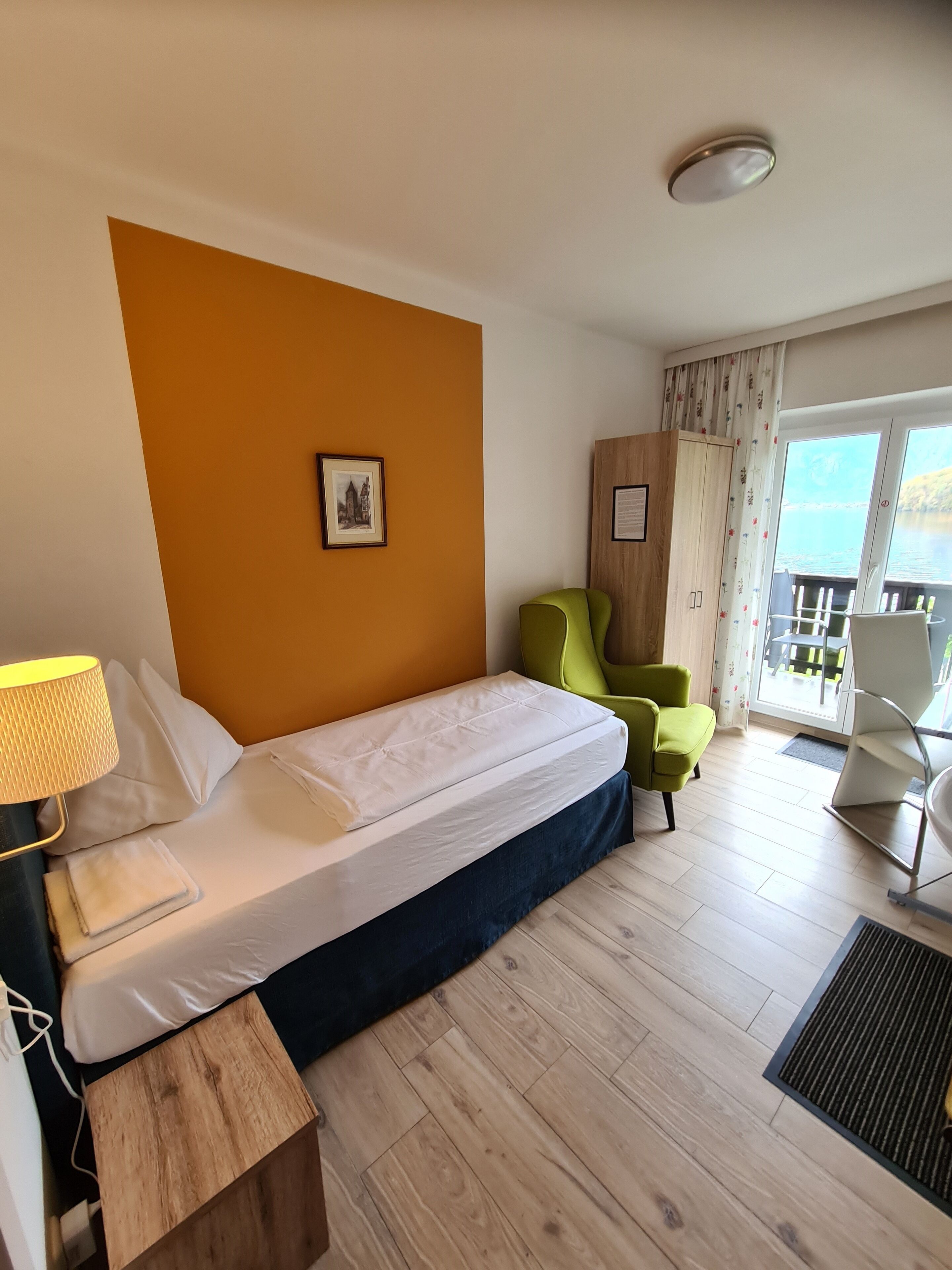 Una habitación de hotel con una cama, una silla verde, una mesita de noche de madera y vistas al exterior.