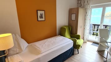 Una habitación de hotel con una cama, una silla verde, una mesita de noche de madera y vistas al exterior.