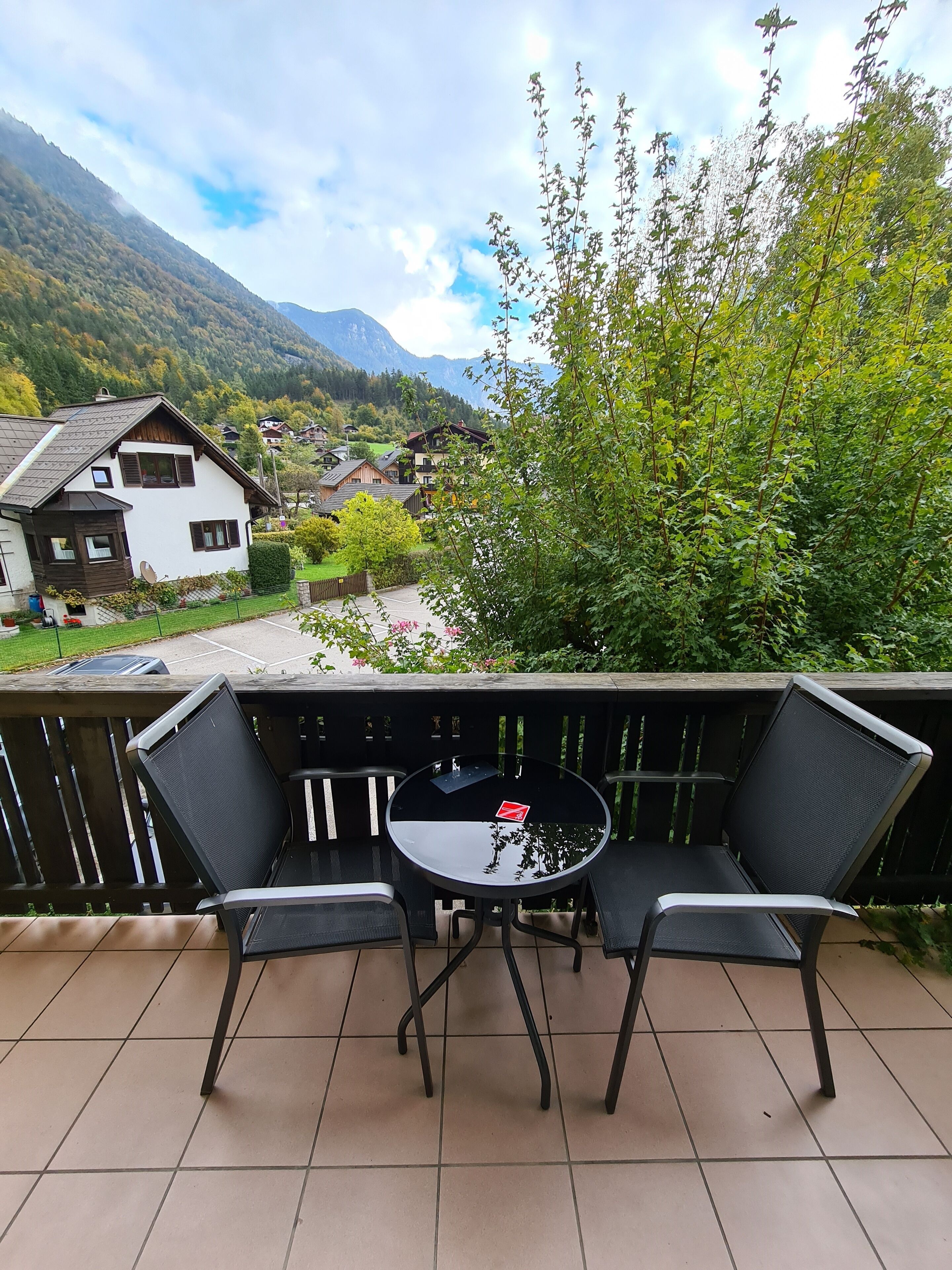 Une terrasse avec deux chaises noires et une table ronde, d’où l’on a vue sur un village et des montagnes.