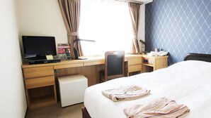 A hotel room with a bed, a desk with a computer, a chair, a small fridge, and a window with curtains. - Takamatsu City Hotel (Takamatsu)