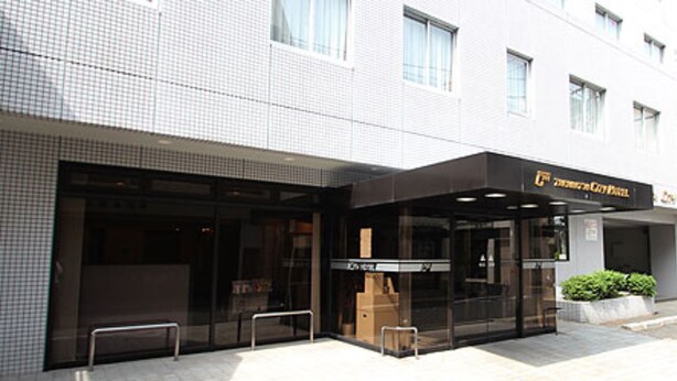 A hotel entrance with a glass facade, a bench outside, and a parking sign. - Takamatsu City Hotel (Takamatsu)
