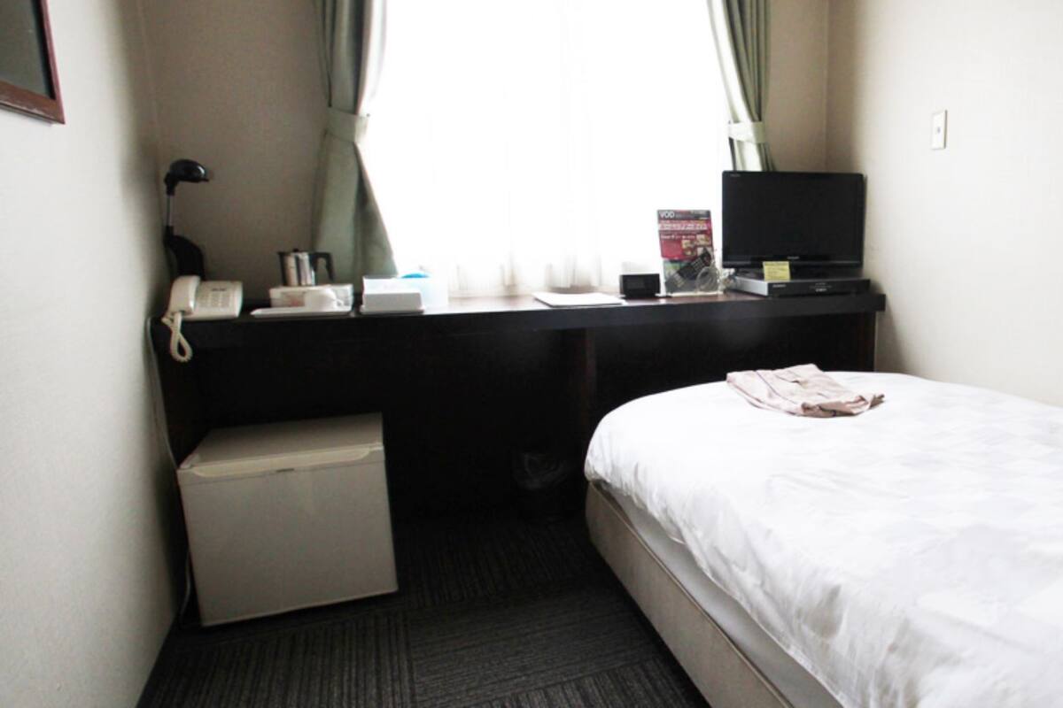 A small hotel room with a single bed, a desk with a computer and a telephone, and a small seating area.