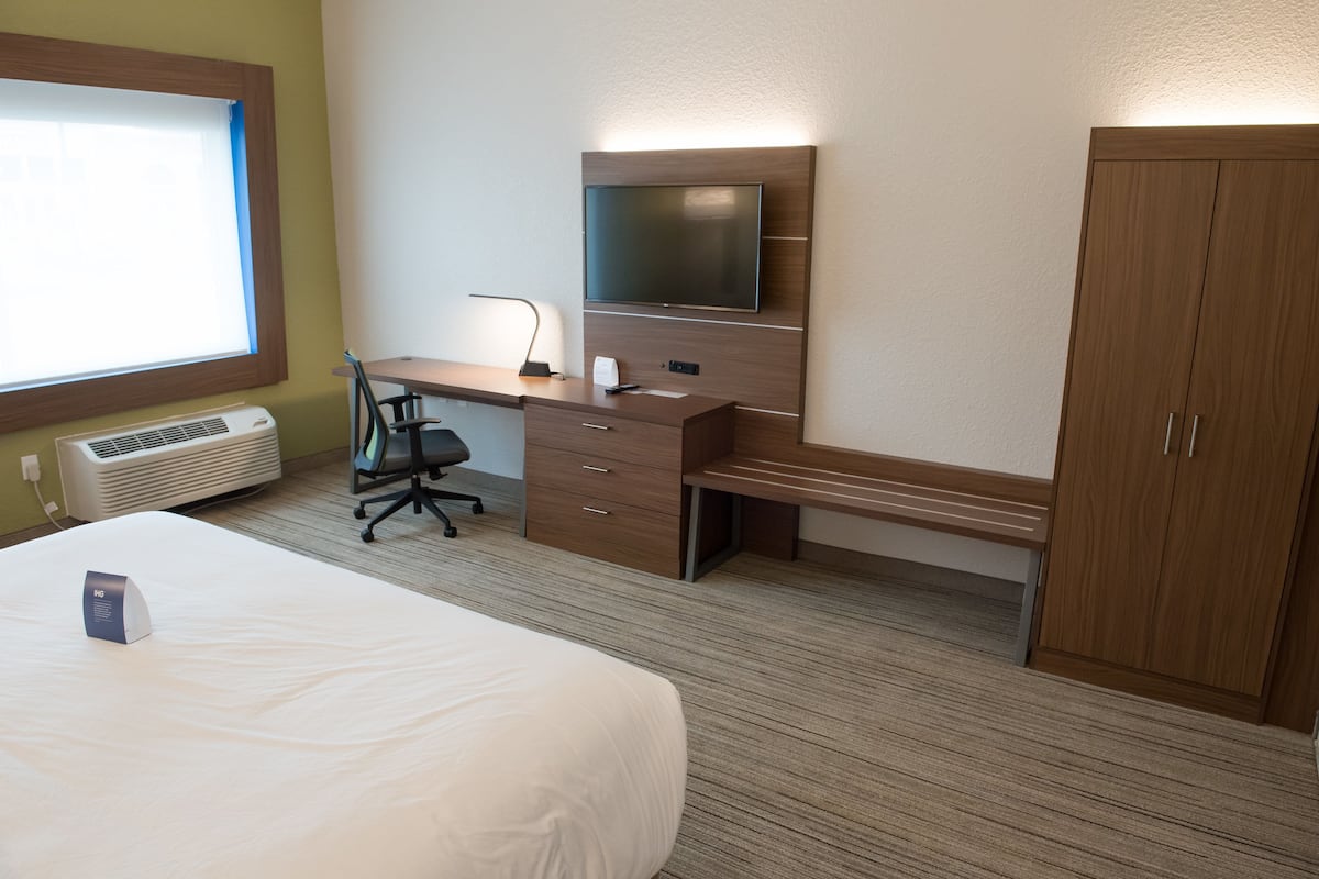A hotel room with a bed, a desk with a chair, a television, and a wardrobe.