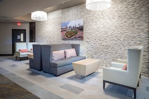 Un vestíbulo con pared de piedra, un sofá gris con cojines estampados, un sillón blanco y una pequeña mesa de madera.