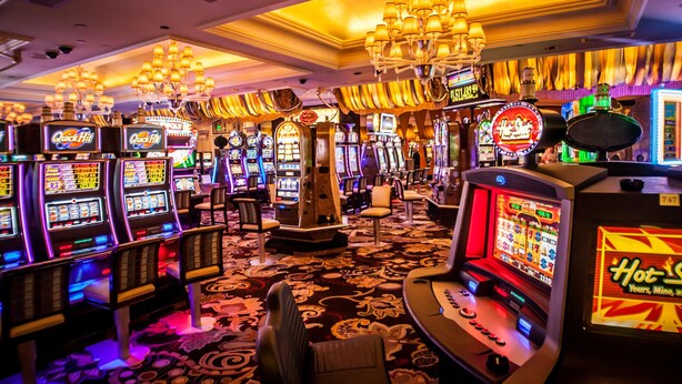 Une salle de casino avec des machines à sous, des lustres et un sol recouvert de moquette.