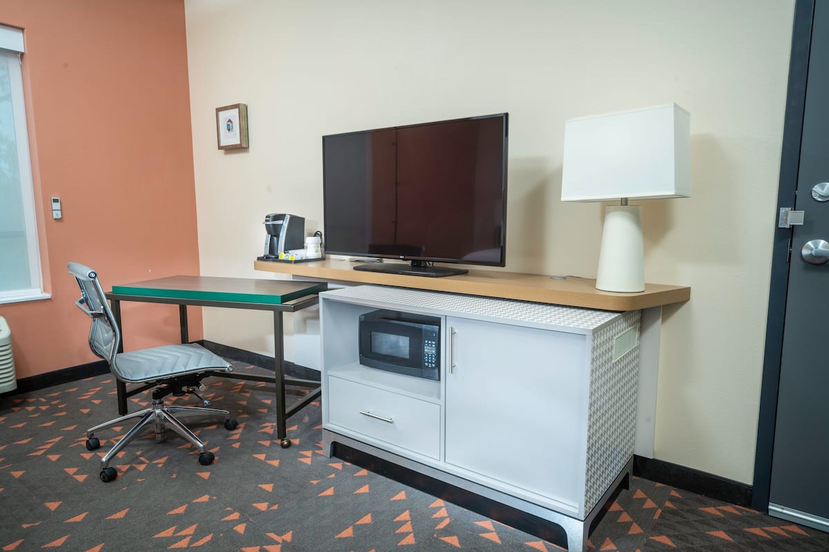 Une chambre d’hôtel équipée d’un bureau, d’une chaise, d’un four à micro-ondes, d’une télévision et d’une lampe.