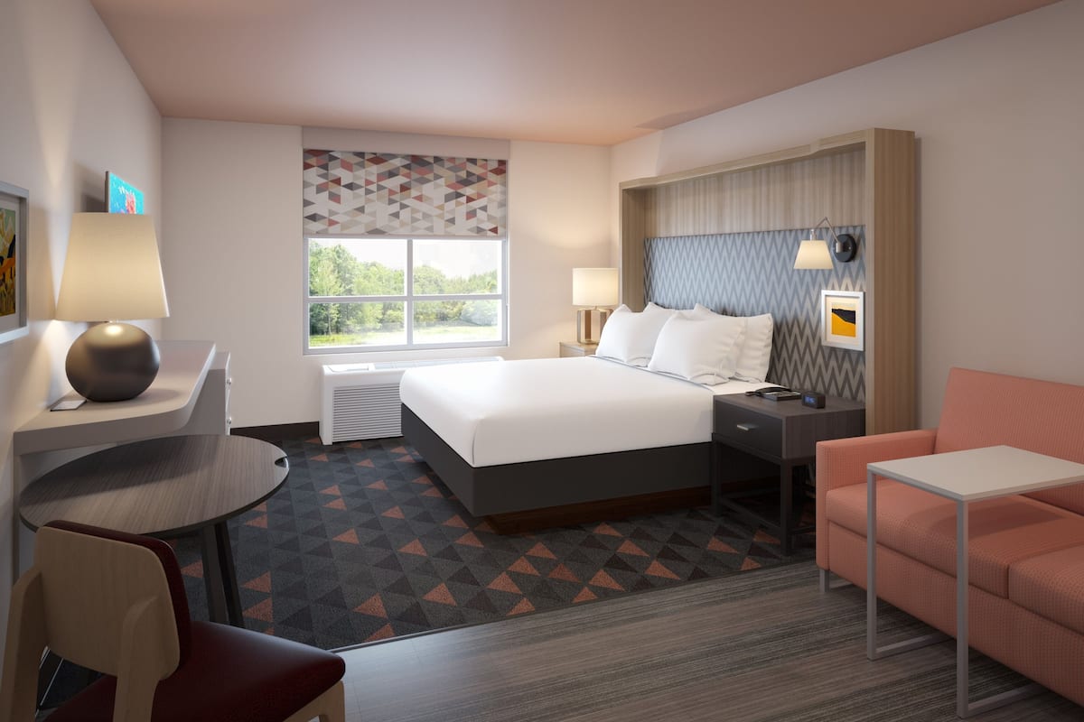 Une chambre d’hôtel comprenant un lit, des tables de chevet, un bureau, une chaise, un canapé et une fenêtre donnant sur un paysage agréable.