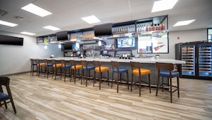 Un espace bar doté d’un long comptoir, de plusieurs tabourets et d’un réfrigérateur.