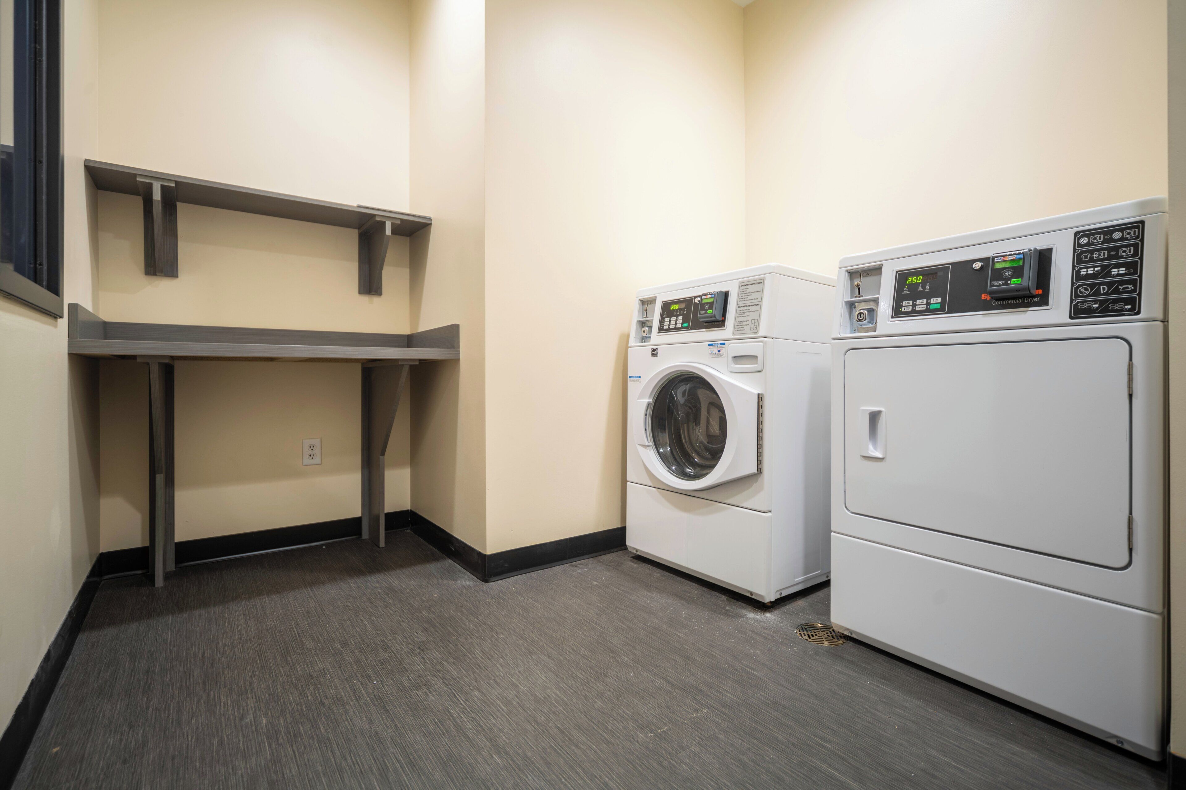A laundry room with two washing machines, a drying machine, and a shelf.