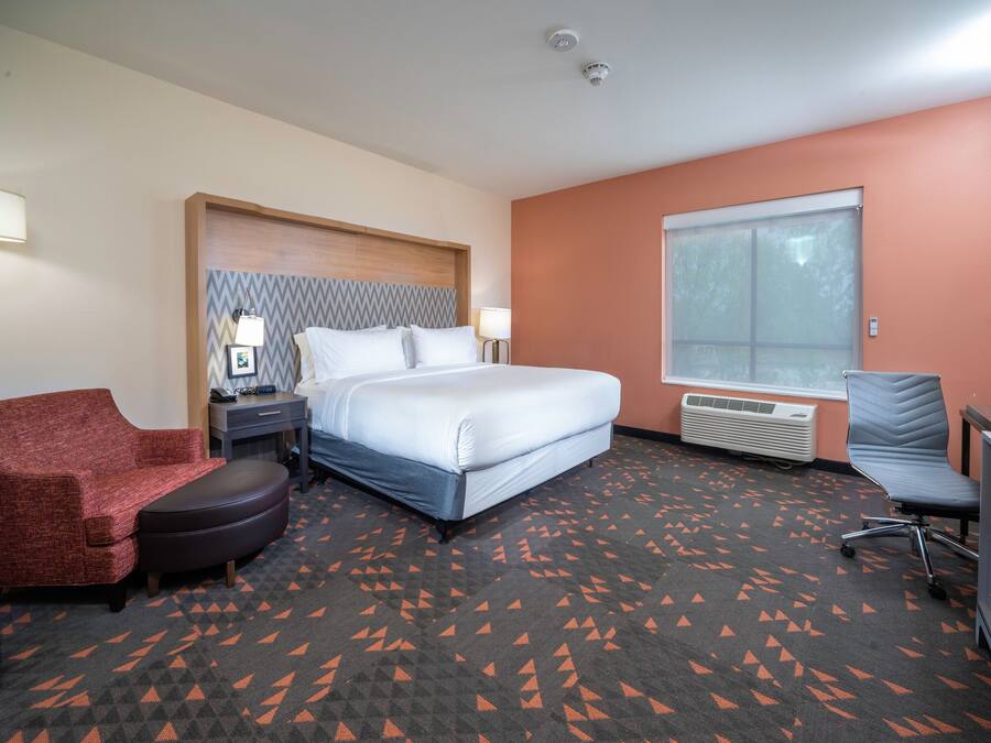 A hotel room with a bed, a red armchair, a desk, and a window.