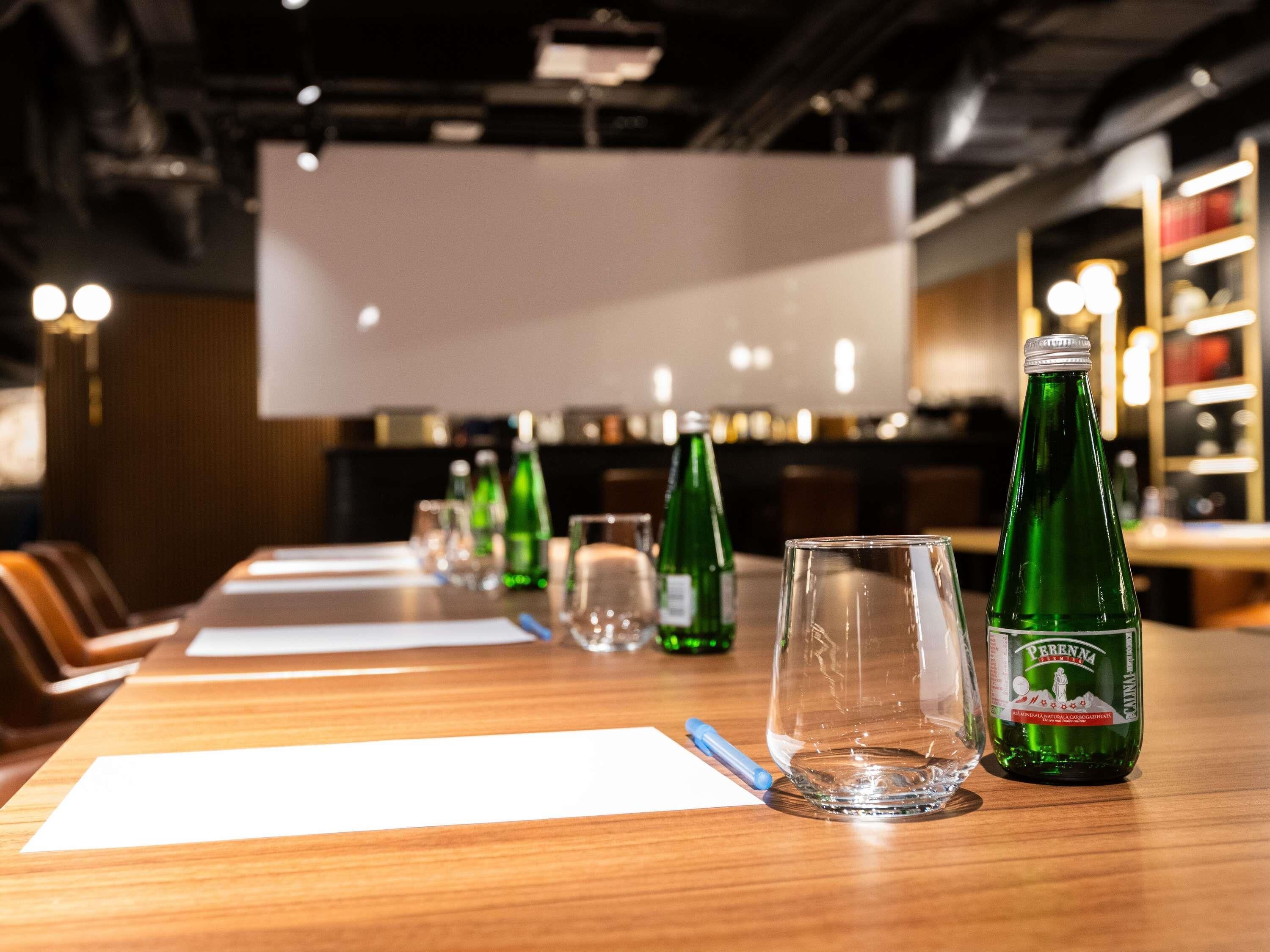 Et konferencemødebord med stole, en flaske Perenna mineralvand og glas.
