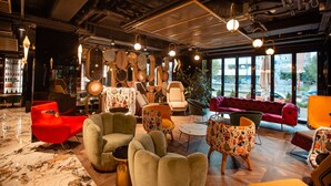 A modern lounge area with various seating options, a large window offering a view of the city, and a bar area with shelves of bottles. - Mercure Timisoara (Timisoara)