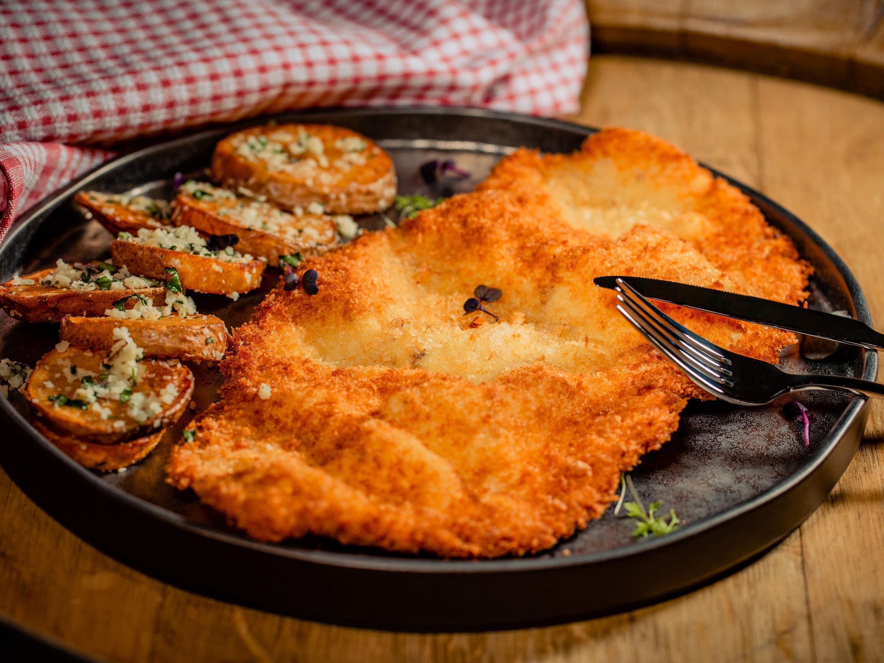 A plate with breaded cutlet, potato slices, and a fork.