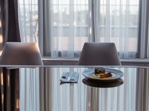 A dining table with a plate of food and cutlery, two chairs, and a window with curtains. - Mercure Timisoara (Timisoara)