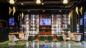 A bar area with a long counter, green upholstered chairs, and shelves of bottles. - Mercure Timisoara (Timisoara)