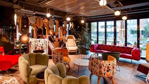A modern interior with a mix of furniture styles, including a green armchair, a patterned ottoman, and a red sofa. - Mercure Timisoara (Timisoara)