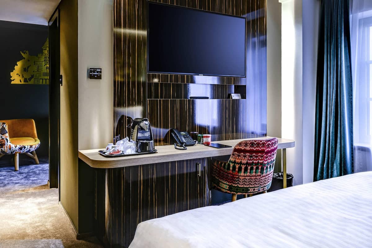 A hotel room with a bed, a desk with a telephone, a coffee maker, and a TV mounted on the wall.