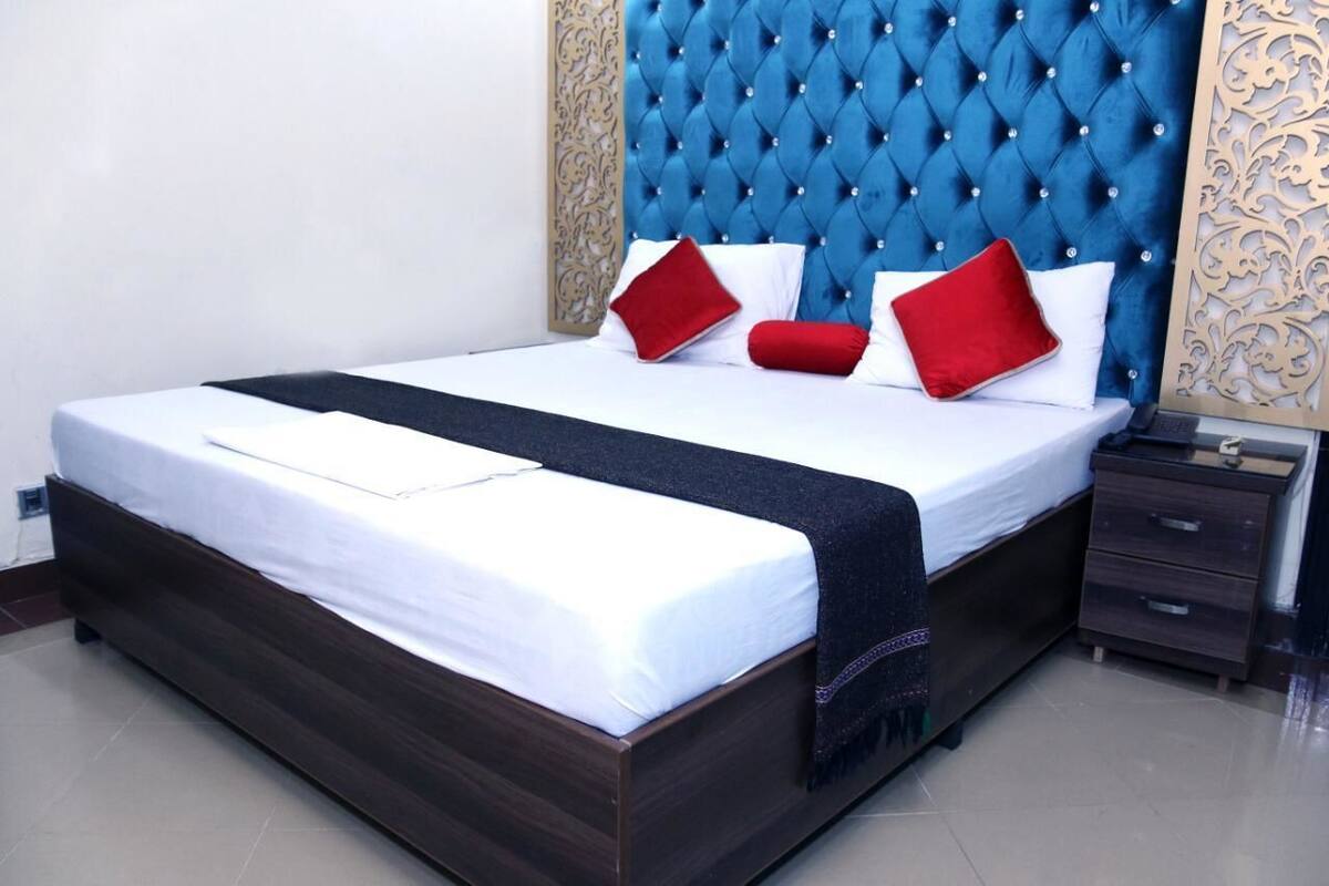 Una cama bien hecha con cabecera tapizada azul, sábanas blancas y almohadas rojas.