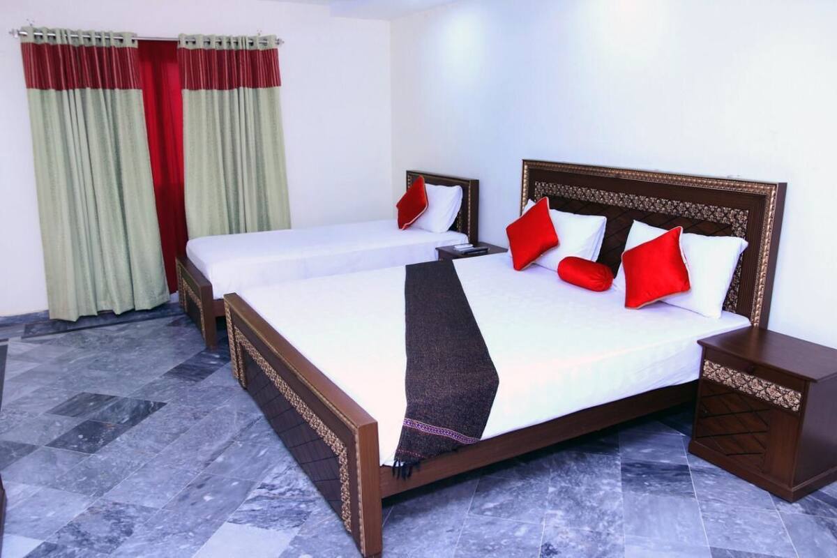 Habitación de hotel con dos camas individuales, cabecero de madera, mesita de noche y suelo de mármol.
