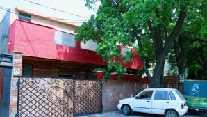 A white car parked in front of a building with a red and beige facade, a metal gate, and potted plants on the roof. - EXECUTIVE PALACE HOTEL LAHORE (Lahore)
