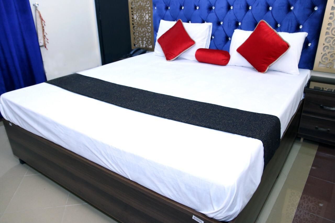A neatly made bed with white and red pillows, a dark headboard, and a wooden frame.