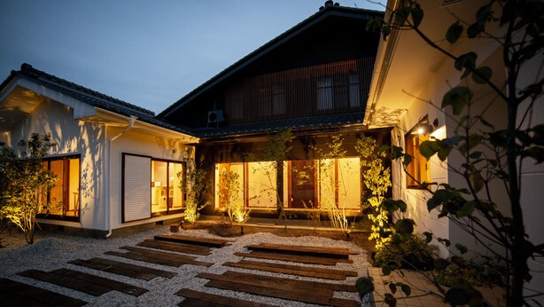 Una casa tradicional japonesa con una terraza de madera y un camino de grava que conduce a la entrada.
