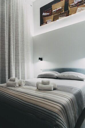 A neatly made bed with striped bedding and rolled towels, a wall-mounted light, and a framed picture above the bed. - Terno su Napoli B&B (Naples)