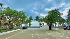 A parking area with a car and motorcycles, surrounded by palm trees and a view of the beach. - My Khe 2 Da Nang Seafront Hotel (Da Nang)