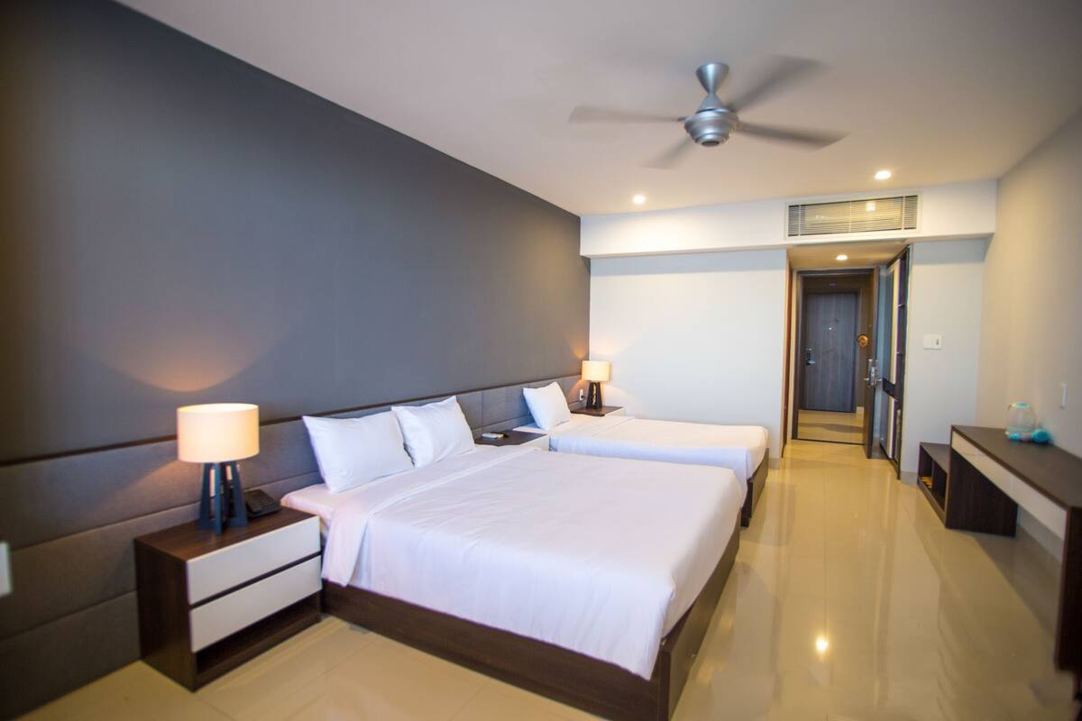 A hotel room with a large bed, bedside tables, a ceiling fan, and a door leading to another room.