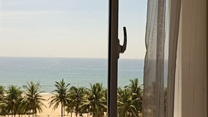 A view of a beach with palm trees and the ocean through a window with a curtain. - My Khe 2 Da Nang Seafront Hotel (Da Nang)