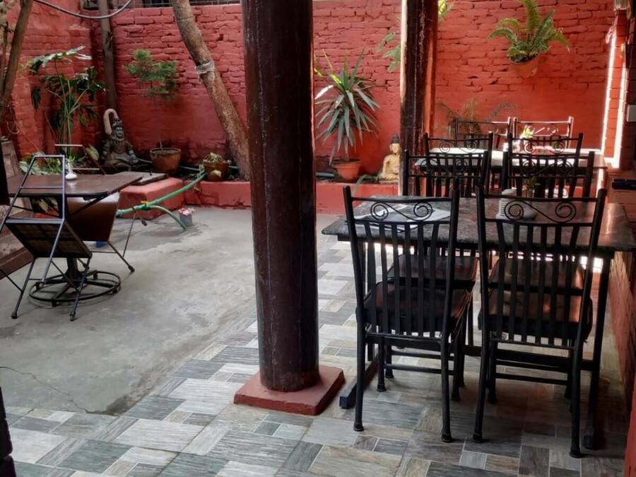 Un patio al aire libre con suelo de baldosas, una columna central y varias mesas y sillas.