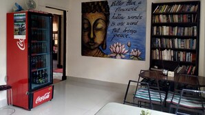 Ett rum med ett kylskåp från Coca-Cola, en bokhylla, en målning av Buddha och en matplats med stolar.